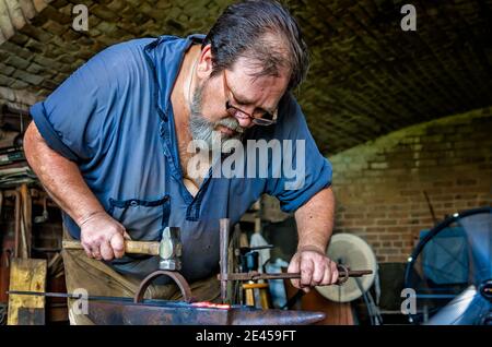 Blacksmith Ralph Oalmann manipulates a heated piece of metal in his shop at Fort Gaines, Aug. 5, 2017, in Dauphin Island, Alabama. Stock Photo