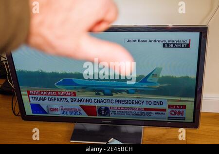 Paris, France - Jan 20, 2021: Male hand showing finger down to tv streaming CNN with main headline Trump departs bringing chaotic presidency to end Stock Photo