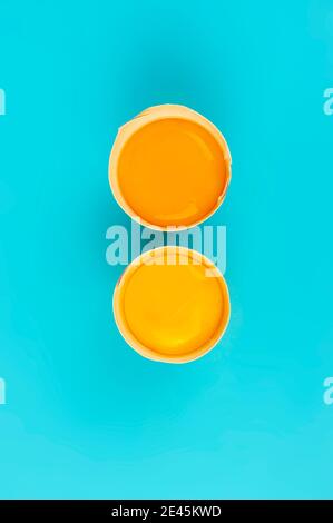 Two raw chicken egg yolks in broken shells vertical on blue background Stock Photo