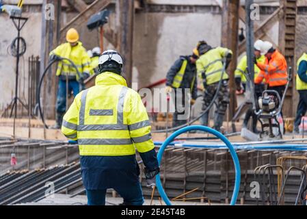 A group of construction workers during concrete casting work, using concrete vibrator for compacting concrete of stiff consistency. Stock Photo