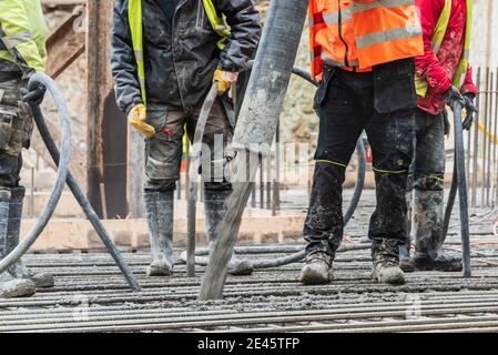 A group of construction workers during concrete casting work, using concrete vibrator for compacting concrete of stiff consistency. Stock Photo