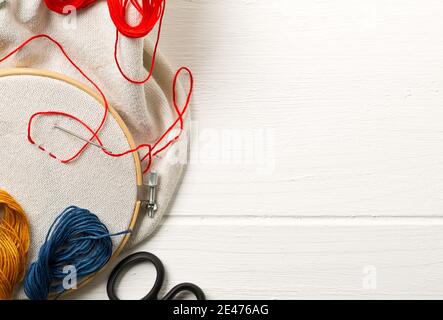 Round stitching or embroidery frame with red stitching and sewing tools on white wooden background, copy space, flat lay top view from above Stock Photo