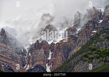 A horizontal image of the rocky mountains looking up at the peaks covered with fog in Alberta Canada. Stock Photo
