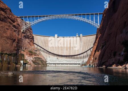 The Glen Canyon Dam holding back Lake Powell and the Glen Canyon Bridge with a clear blue sky background as seen from the surface of the Colorado Rive Stock Photo