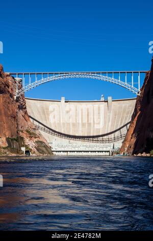 The Glen Canyon Dam holding back Lake Powell and the Glen Canyon Bridge with a clear blue sky background as seen from the surface of the Colorado Rive Stock Photo