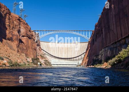 The Glen Canyon Dam holding back Lake Powell and the Glen Canyon Bridge with a clear blue sky background as seen from the surface of the Colorado Rive Stock Photo