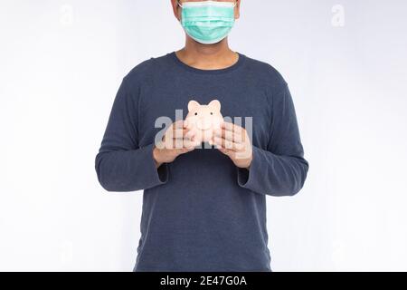 Asian man wearing a face mask holding pink piggy bank, isolated on a white background Stock Photo