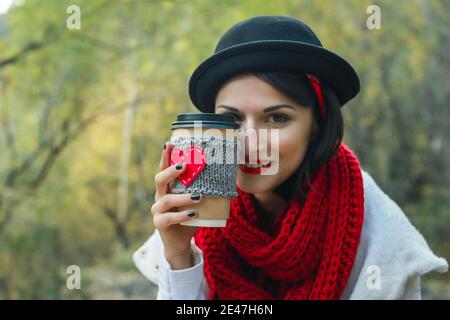 Young woman in a black hat drinks coffee from cozy cup on the nature. Bright smile and good mood. Stock Photo