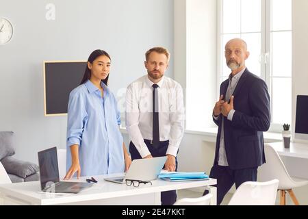 Group of serious diverse employees standing in office of their company looking at camera Stock Photo