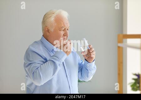 White-haired senior man taking prescribed medicine with a glass of fresh water at home Stock Photo