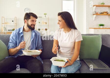 Young smiling couple office workers sitting on sofa and enjoying healthy boxed food Stock Photo