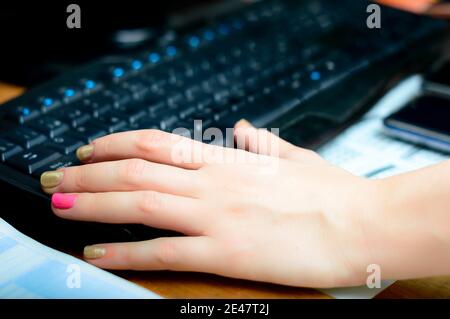 Closeup shot of a female with colored nails typing on a computer keyboard in an office Stock Photo