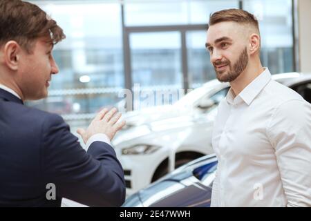 Charming handsome man talking to car dealer while choosing new automobile to buy Stock Photo
