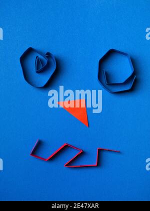 A face made from color paper on blue background Stock Photo