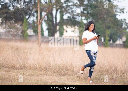 beautiful african lady walking alone in a park, smiling while using her phone Stock Photo