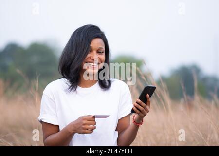 pretty young african woman smiling while holding a credit card and her phone Stock Photo