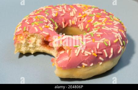 Pink sweet doughnut or donut with colored sprinkles on a blue background. Bitten off American bagel. Stock Photo