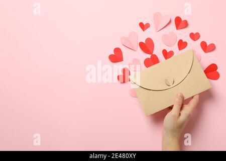 Female hand holding an envelope with decorative hearts on pink, a sweet Valentines Day love letter in pastel tones Stock Photo