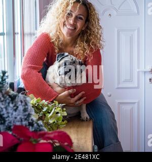 Cheerful dog owner beautiful adult female at home hugging her pug with love and tenderly - concept of people and animals pet therapy - adorable little Stock Photo