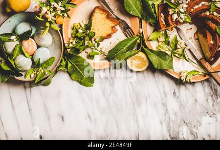Easter holiday dinner table setting. Flat-lay of Easter Eggs, Lemon cake with citrus tree blossom branches and black tea over white marble table background, top view, copy space. Easter greeting card Stock Photo