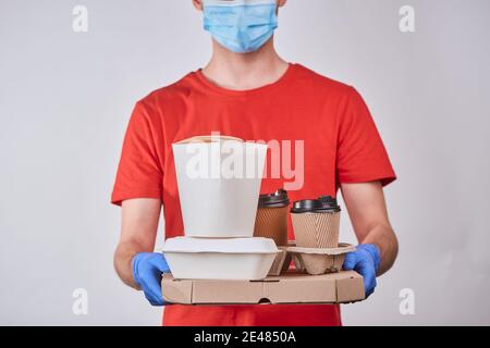 Delivery man holding a box of pizza, wok and cups of coffee Stock Photo