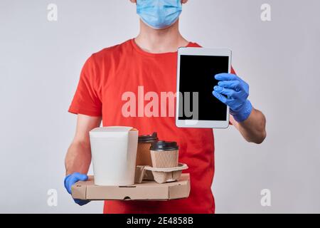 Delivery man showing a tablet with app and holding a pile of boxes with food Stock Photo