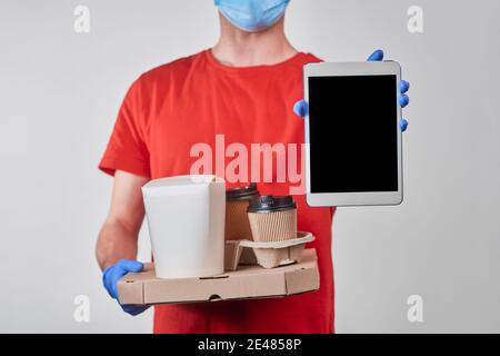 Delivery man showing a tablet and holding a pile of boxes with food Stock Photo