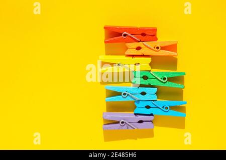 Mood-boosting color concept, multi-colored wooden multi-colored clothespins in a row on a yellow paper background. Creative minimalistic design, flat Stock Photo