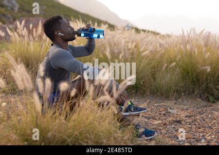Portrait of fit african american man in sportswear resting drinking water in tall grass Stock Photo