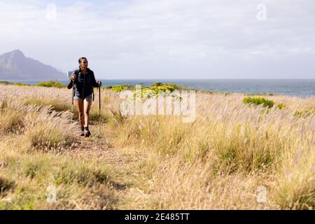 Fit african american woman wearing backpack nordic walking on coast Stock Photo