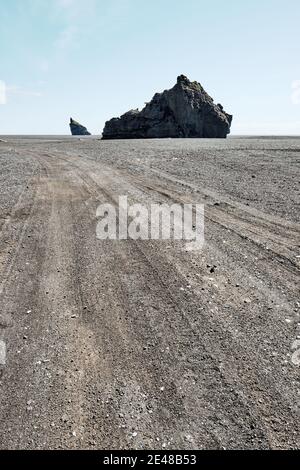 Tyre tracks and the Arnardrangur rock pillar in the strange lunar like black sand landscape of Mýrdalssandur near Vik south Iceland. Stock Photo