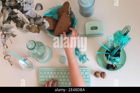 PETRER, SPAIN - Jul 17, 2019: Different turquoise colored objects like computer keyboard, pens and paper clips; and hand grabbing a piece of bread Stock Photo