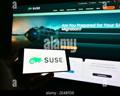 Person holding smartphone with logo of German software developer SUSE Software Solutions Germany GmbH on display. Focus on left of phone screen. Stock Photo