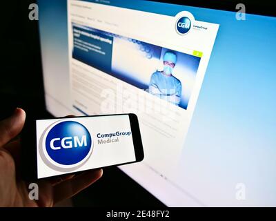 Person holding smartphone with logo of German software developer CompuGroup Medical on screen. Focus on center of mobile phone display. Stock Photo