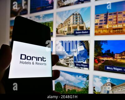 Person holding smartphone with logo of German hotel chain Dorint GmbH on screen in front of company website. Focus on lift of mobile phone display. Stock Photo