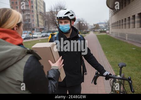 Cycling courier wearing medical face mask, delivering package to a female client Stock Photo