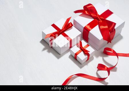 Minimalist elegant three New Year white gift boxes with red bow on white wood board as border. Stock Photo