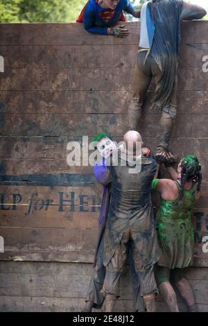 Muddy legs slipping and sliding all over the place as they attempt to climb a slippery wooden barrier during a Tough Mudder endurance event Stock Photo