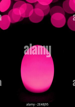 Shining Hot Pink Egg Shaped Table Lamp with Abstract Blurred Lights on Black Background Stock Photo