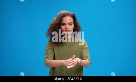 Using her hands to communicate pretty african american girl. Curly haired young woman showing hello sign talking on camera isolated on blue background Stock Photo