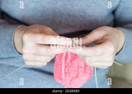 Close up of hands of unrecognizable woman knitting handmade clothes with spokes using pink wool yarn. Concept of leisure activity. Stock Photo
