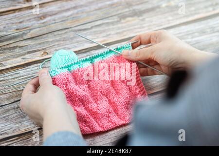 Close up of hands of unrecognizable woman knitting handmade clothes with spokes using pink wool yarn. Concept of leisure activity. Stock Photo
