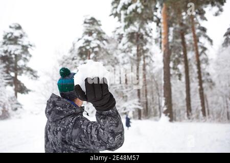 A young man with a snowball in his hand is having fun, swinging for a throw. Winter family and friendly games and entertainment in the forest with sno Stock Photo