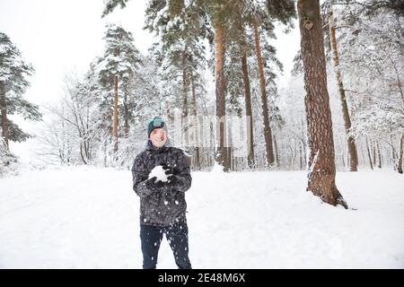 A young man with a snowball in his hand is having fun, swinging for a throw. Winter family and friendly games and entertainment in the forest with sno Stock Photo