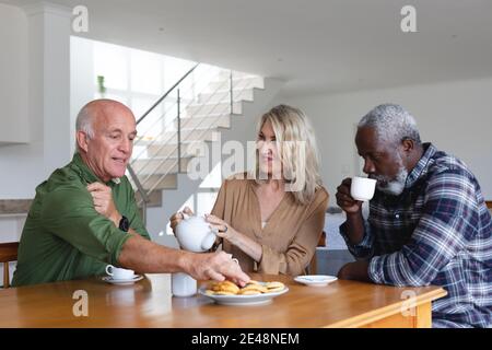 Senior caucasian and african american couples sitting by table drinking tea at home Stock Photo