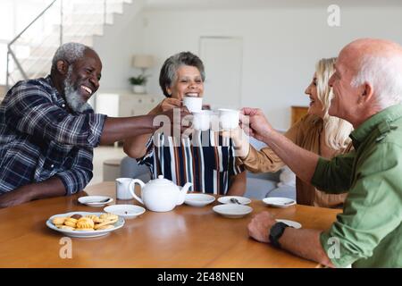 Senior caucasian and african american couples sitting by table drinking tea at home Stock Photo
