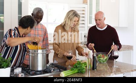 Senior caucasian and african american couples making pasta and salad at home Stock Photo