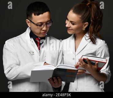 Young smiling couple woman and man doctors in white uniform standing and looking at professional books Stock Photo