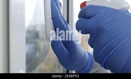 Close Up Man Hands with Protection Gloves Cleaning a Window Using Sprayed Liquid Disinfecting Against Viruses Contamination Stock Photo