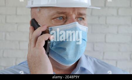 Engineer with Safety Helmet and Medical Face Mask Talking to Mobile Stock Photo